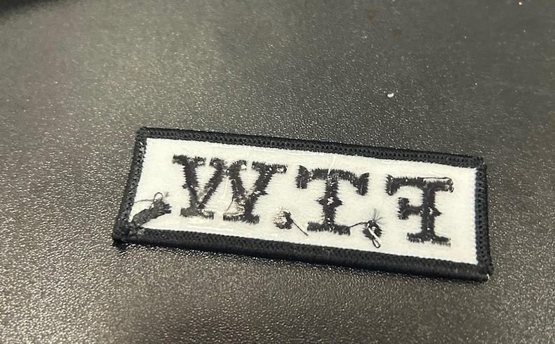 May include: Black and white embroidered patch with the letters "WTF" in white on a black background.