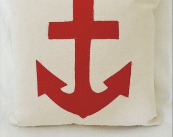 May include: A white pillow with a red anchor design. The anchor is a simple, stylized design with a cross at the top and two points at the bottom.