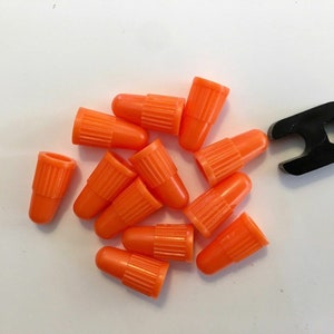 May include: A close-up of a pile of orange valve stem caps and a black valve stem removal tool.