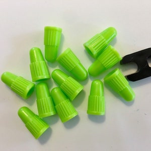 May include: A group of 13 bright green valve stem caps and a black valve stem cap removal tool.