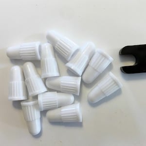 May include: A close-up of a pile of white plastic caps with a black plastic tool in the background.