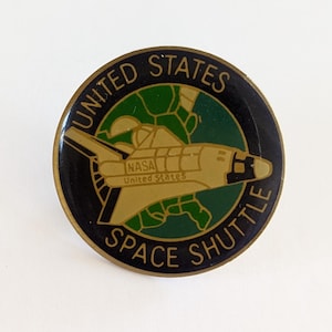Op de afbeelding: Ronde pin met een zwarte rand met een goudkleurig ruimteveer-ontwerp. De pin bevat de tekst "UNITED STATES SPACE SHUTTLE" in groen en goud, met "NASA United States" op de shuttle.