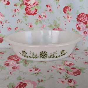 Peut inclure: Un plat à four ovale blanc avec un motif floral vert. Le plat a une finition lisse et brillante et deux petites poignées. Le motif floral se compose de fleurs et de feuilles stylisées.