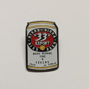 May include: A metal pin shaped like a beer can. The pin is silver, black, red, and gold. The text on the pin reads "33 Export Beer" and "Biere Blonde, Fine & Légère alc 4.8% vol".
