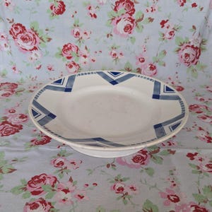 May include: A white ceramic plate with a blue and white geometric design. The plate has a raised edge and a flat base.