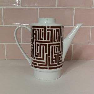 May include: White ceramic teapot with a brown geometric pattern. The teapot has a spout and a handle.