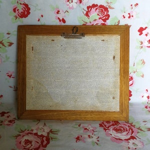 May include: A wooden picture frame with a light brown finish. The frame has a metal clip on the top and a white mesh backing.