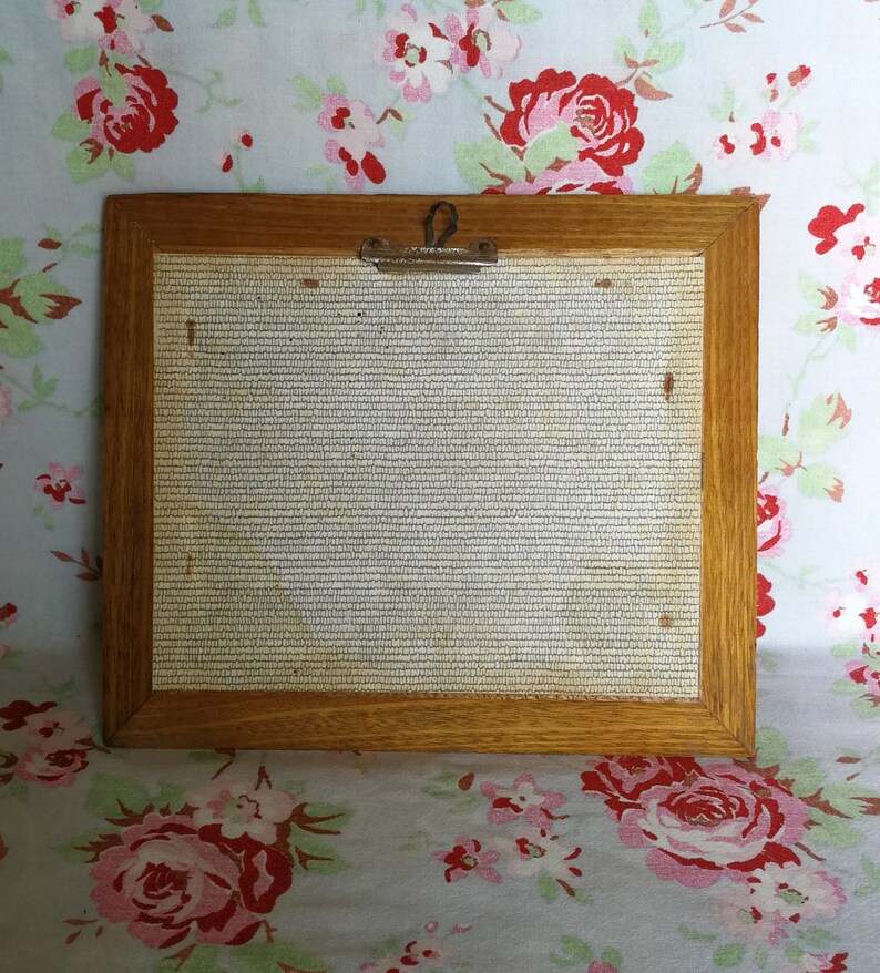 May include: A wooden picture frame with a light brown finish. The frame has a metal clip on the top and a white mesh backing.