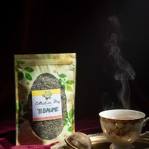 May include: A still life image featuring a bag of loose leaf tea labeled "Ti Baume" next to a teacup with steam rising. A tea infuser and a spoon rest on a decorative tray. The background is a dark red.