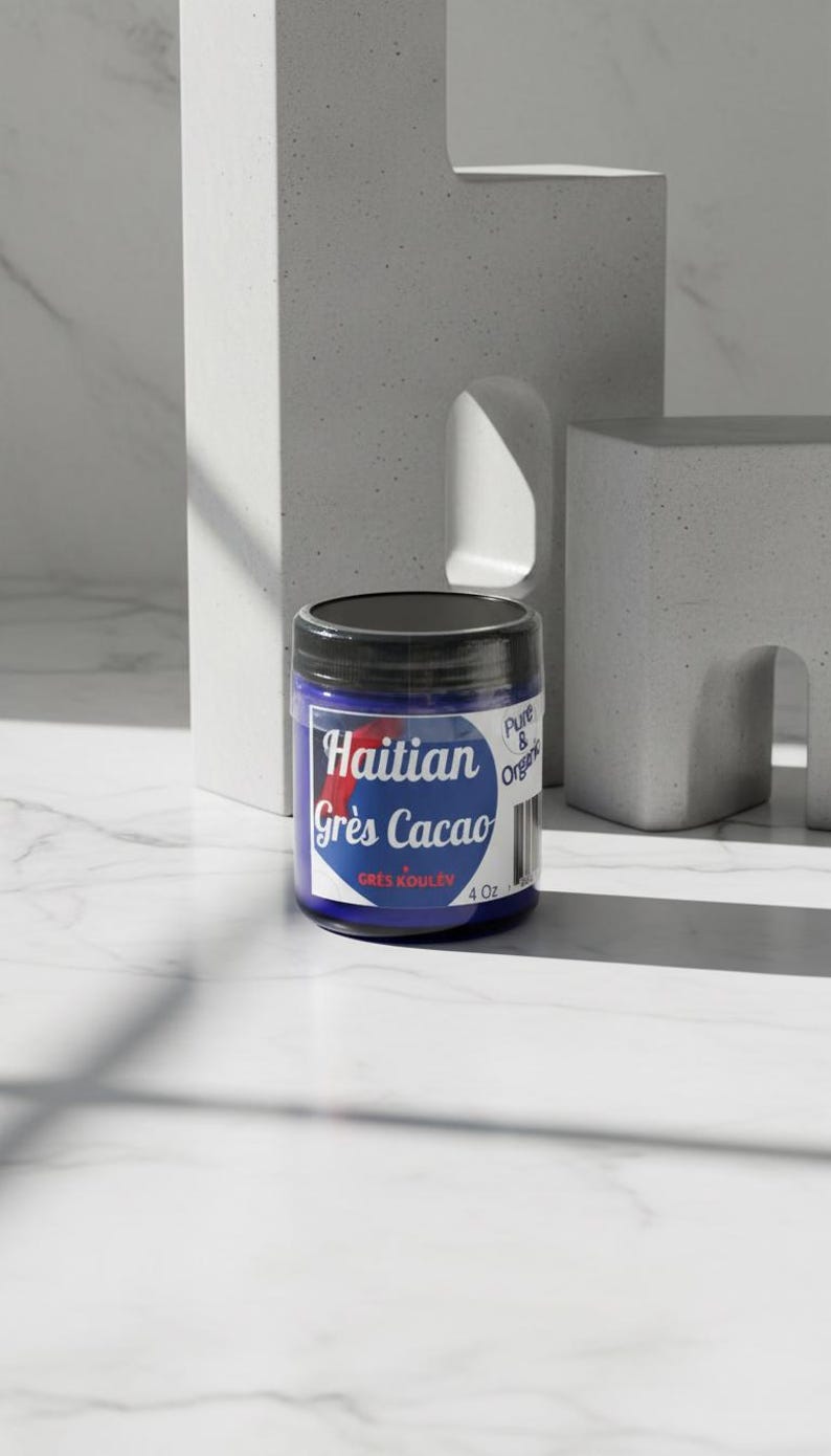 Op de afbeelding: Een blauwe pot met een zwart deksel, met het opschrift "Haitian Gr&egrave;s Cacao" met een rode accent. De pot bevat 113g product en staat tegen een minimalistische, getextureerde achtergrond.