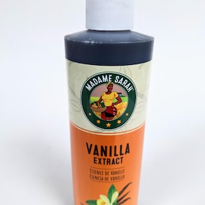 May include: A dark brown glass bottle of Madame Sarah Vanilla Extract. The label is orange with a green circle featuring a woman in a yellow dress holding a basket of fruit. The text on the label reads "Madame Sarah" and "Vanilla Extract".