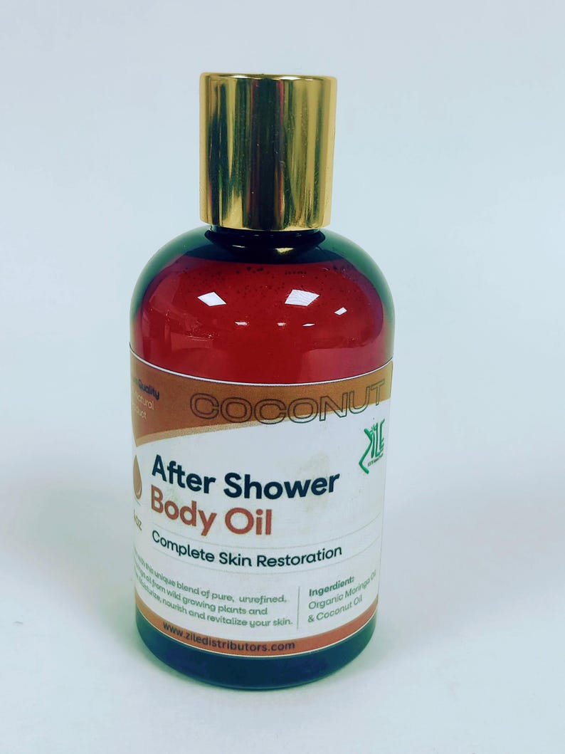 May include: A brown glass bottle with a gold lid and a white label that reads "COCONUT After Shower Body Oil Complete Skin Restoration". The label also includes the text "Ingredients: Organic Monoi Oil, Organic Coconut Oil & Coconut Oil" and the website "www.ziledistributors.com".