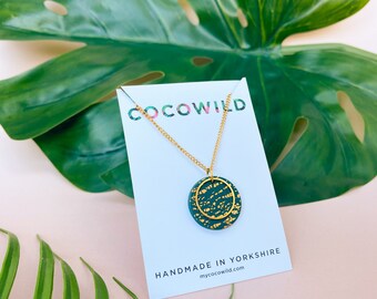 May include: A gold chain necklace with a green and gold circular pendant. The pendant has a textured surface and a gold outline. The necklace is displayed on a white card with the text "COCOWILD" and "HANDMADE IN YORKSHIRE" mycocowild.com.