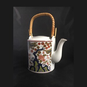 May include: White teapot with a floral design and a woven bamboo handle. The teapot has a spout and a lid.