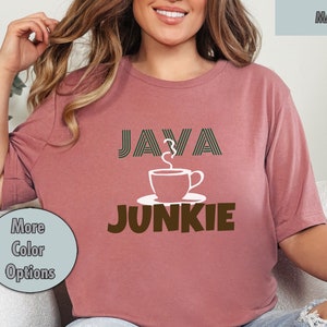 Puede incluir: Una camiseta corta de color malva con el texto "JAVA JUNKIE" en marrón y blanco. El texto "JAVA" está en una fuente de rayas y una taza de café blanca con vapor está entre las palabras.