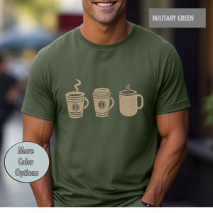 Può includere: Una maglietta verde con una grafica di tre tazze di caffè. Le tazze sono marroni e hanno un contorno bianco. Il testo "MILITARY GREEN" è nell'angolo in alto a destra dell'immagine.