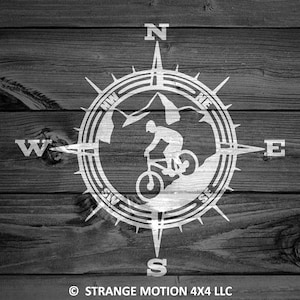 Puede incluir: Diseño de brújula en blanco y negro con una silueta de montaña y una persona montando una bicicleta. La brújula apunta al norte, sur, este y oeste. El texto "STRANGE MOTION 4X4 LLC" está en la parte inferior de la imagen.