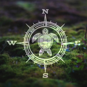 May include: A compass with a sea turtle design on a green mossy background. The compass points north, south, east, and west. The compass is surrounded by a circle with the letters N, S, E, W, NE, NW, SE, and SW.