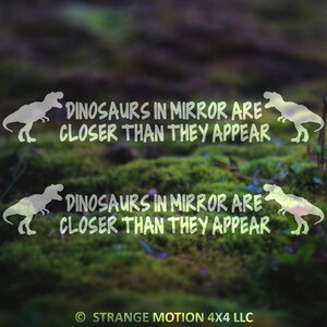 May include: A green mossy background with two white silhouettes of dinosaurs and the text "Dinosaurs in mirror are closer than they appear" repeated twice. The text is in a handwritten style font. The copyright text "STRANGE MOTION 4X4 LLC" is at the bottom of the image.