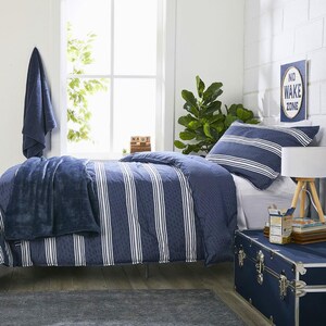 May include: A navy blue and white striped comforter set on a bed, with a matching pillow. A navy blue blanket is draped over the bed. A navy blue trunk and a sign that says "No Wake Zone" are also in the room.