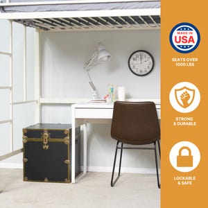 May include: A black trunk with gold-colored accents and a lock sits next to a white desk with a brown chair. A white desk lamp and a clock are on the wall. The image also includes the text "MADE IN USA", "SEATS OVER 1000 LBS", "STRONG & DURABLE", and "LOCKABLE & SAFE".