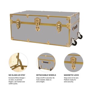 May include: A gray trunk with gold-colored accents, including corner protectors, latches, and a central lock. The trunk has detachable wheels and a magnetic lock. Text on the image reads: "NO SLAM LID STAY", "DETACHABLE WHEELS", and "MAGNETIC LOCK".