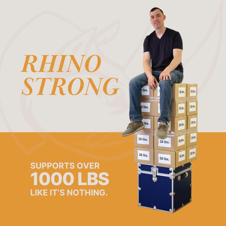 May include: A man sits atop a stack of cardboard boxes and a blue trunk. The boxes are labeled "38 lbs." and the image includes the text "RHINO STRONG" and "SUPPORTS OVER 1000 LBS LIKE IT'S NOTHING."