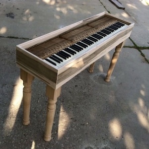 Könnte beinhalten: Eine Holztastatur mit natürlicher Holzoptik und einer Reihe von weißen und schwarzen Tasten. Die Tastatur steht auf einem Ständer mit gedrehten Beinen.