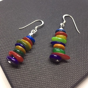 May include: A pair of silver dangle earrings with colourful glass beads. The beads are stacked in a tower shape and are red, orange, yellow, green, blue and purple.