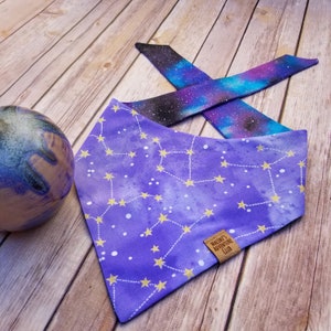 Puede incluir: Bandana morada con un patr&oacute;n de constelaci&oacute;n y estrellas doradas. La bandana tiene una etiqueta de cuero marr&oacute;n que dice "Macie's Adventure Club".