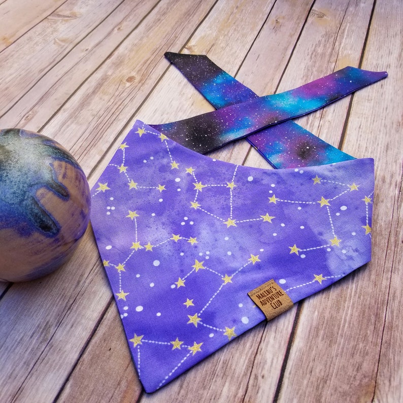 Puede incluir: Bandana morada con un patr&oacute;n de constelaci&oacute;n y estrellas doradas. La bandana tiene una etiqueta de cuero marr&oacute;n que dice "Macie's Adventure Club".