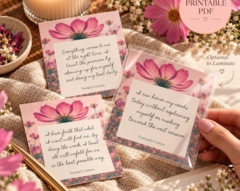 May include: Three square cards featuring pink cosmos flower illustrations and printed affirmations. The cards display text including Everything comes to me at the right time, I can honour my needs today, and I have faith that what I want will find me.