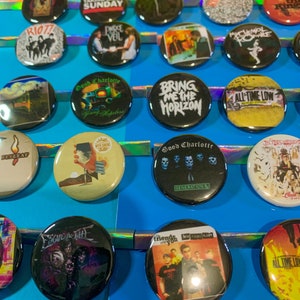 Puede incluir: Una colecci&oacute;n de botones redondos y coloridos con varios logotipos de bandas y portadas de &aacute;lbumes. Los botones incluyen bandas como My Chemical Romance, Good Charlotte, All Time Low, Bring Me The Horizon y Taking Back Sunday.