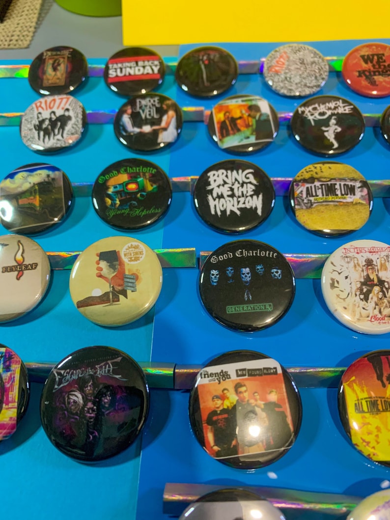 Puede incluir: Una colecci&oacute;n de botones redondos y coloridos con varios logotipos de bandas y portadas de &aacute;lbumes. Los botones incluyen bandas como My Chemical Romance, Good Charlotte, All Time Low, Bring Me The Horizon y Taking Back Sunday.