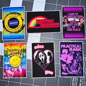 May include: A collection of rectangular stickers with various designs and text. One sticker features a Blockbuster logo with "BE KIND PLEASE REWIND". Other stickers include "READING RAINBOW", "DAZED AND CONFUSED", and "PRACTICAL MAGIC".