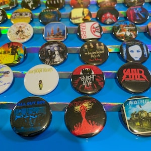 Puede incluir: Una colecci&oacute;n de botones redondos con portadas de &aacute;lbumes de varias bandas, incluyendo Fall Out Boy, Hawthorne Heights, Tonight Alive, The All-American Rejects y Evanescence.