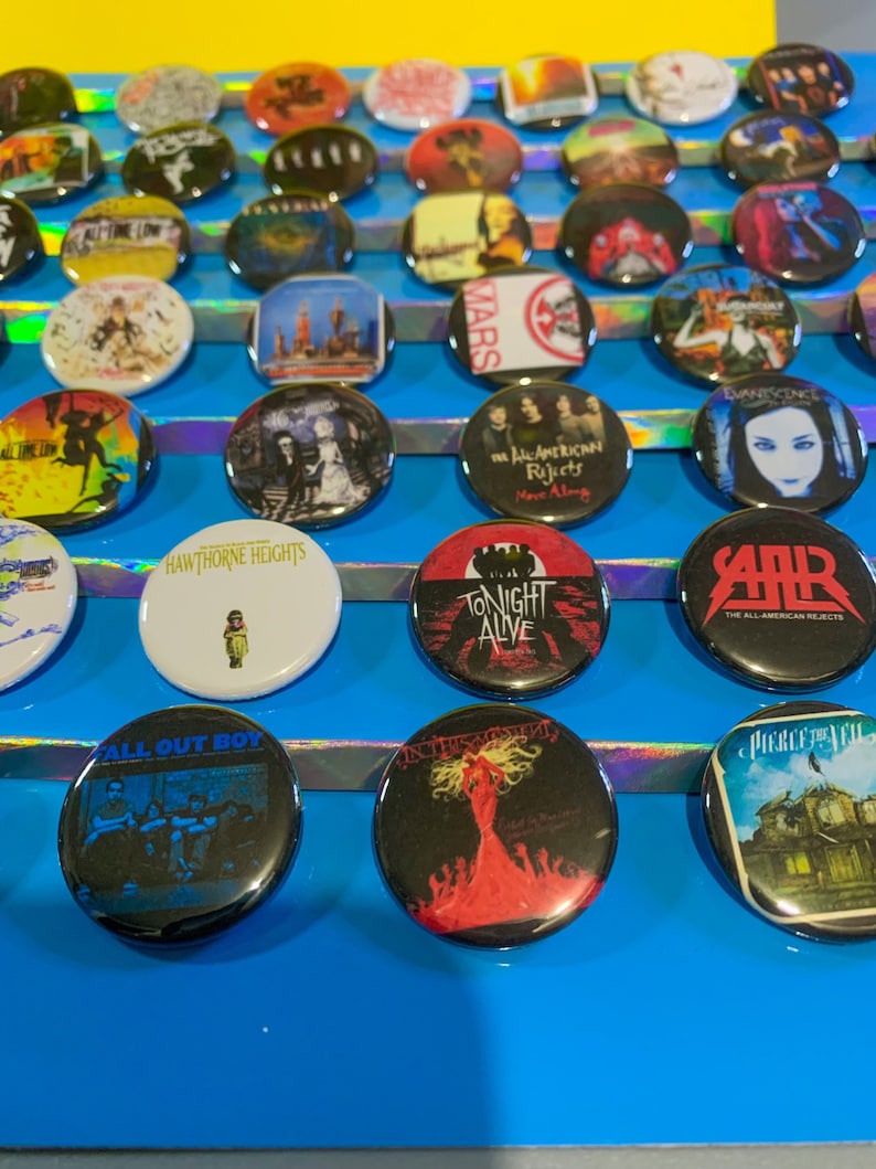 Puede incluir: Una colecci&oacute;n de botones redondos con portadas de &aacute;lbumes de varias bandas, incluyendo Fall Out Boy, Hawthorne Heights, Tonight Alive, The All-American Rejects y Evanescence.