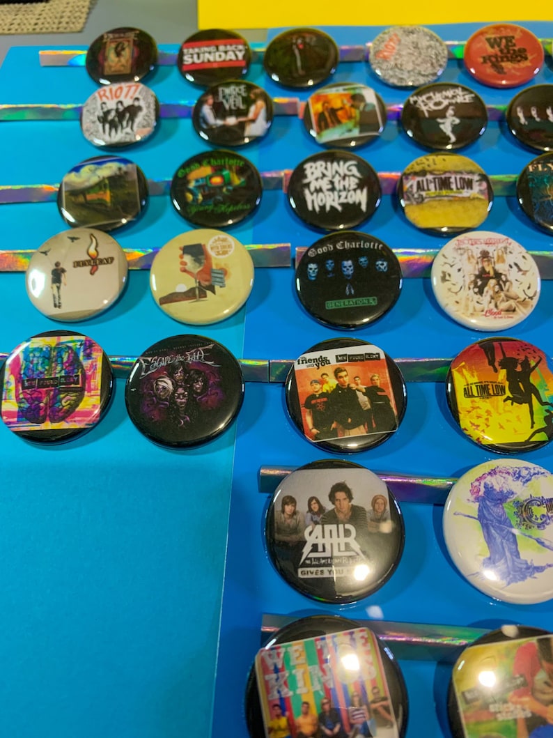 Puede incluir: Una colecci&oacute;n de botones redondos y coloridos con varios logotipos de bandas y portadas de &aacute;lbumes. Los botones incluyen bandas como "Bring Me The Horizon", "Good Charlotte", "All Time Low", "We The Kings", "My Chemical Romance" y "Rise Against".