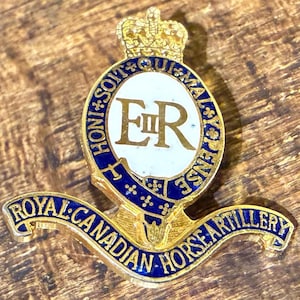May include: A gold-colored Royal Canadian Horse Artillery badge with blue and white enamel details. The badge features a crown, the initials "ER", and the text "Royal Canadian Horse Artillery".