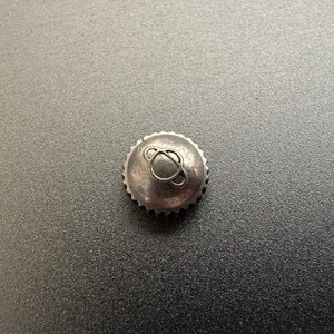 May include: A silver watch crown with a small, circular design on top.