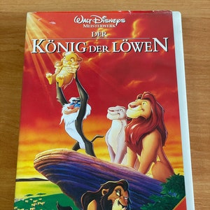 Puede incluir: Una caja de cinta VHS con un fondo rojo y una escena de puesta de sol. El título "KÖNIG DER LÖWEN" está impreso en letras blancas. La imagen muestra a Simba, Mufasa, Nala y Rafiki de la película de Disney El Rey León. El texto "Walt Disneys Meisterwerk" está impreso en letras blancas. El texto "Ausgezeichnet mit 2 OSCARS®!" está impreso en letras blancas sobre un fondo rojo.