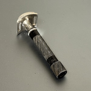 May include: A silver and black safety razor with a textured black handle. The handle has the word "GEM" printed on it.