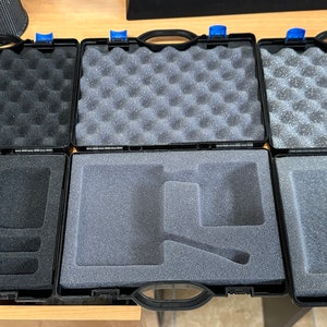 May include: Six open black cases with foam inserts. The top three cases have textured foam, while the bottom three have custom-cut foam inserts. Each case has a black handle and blue accents.
