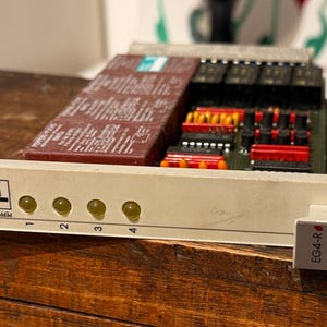 以下が含まれることがあります： 「4p」のロゴと4つの黄色のインジケーターライトが付いた白いフロントパネルを備えた、ヴィンテージの電子回路基板。基板には赤、黒、黄色のコンポーネントと茶色の長方形のモジュールがあります。小さな白いコネクタが取り付けられています。