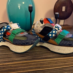 May include: A pair of colorful platform sneakers with white polka dots, green, blue, and brown accents. The sneakers have multiple straps and buckles.