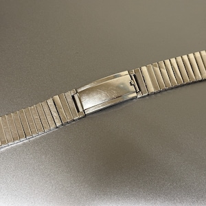 May include: A silver metal watch band with a clasp. The band is made of many small, linked pieces.