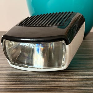 Puede incluir: Una linterna vintage negra y blanca con una lente transparente. La linterna tiene una parte superior acanalada y una base blanca.