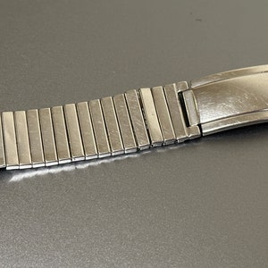 May include: A silver watch band with a clasp. The band is made of many small, linked pieces.