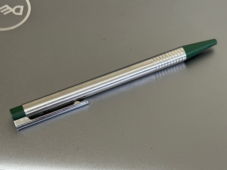 Puede incluir: Un bol&iacute;grafo plateado con una punta verde y una banda verde cerca de la parte inferior. El bol&iacute;grafo tiene un agarre texturizado.