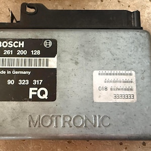 May include: A silver Motronic control unit with black labels from Bosch. The labels include the text "BOSCH", "Made in Germany", and "GM". The unit has a black plastic top.